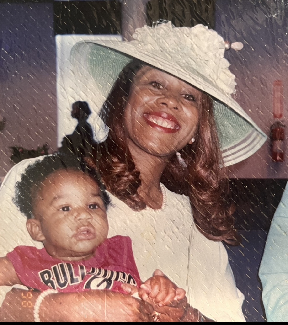 Mary in a wide-brim white hat holding her grandbaby in a Bulldogs jersey