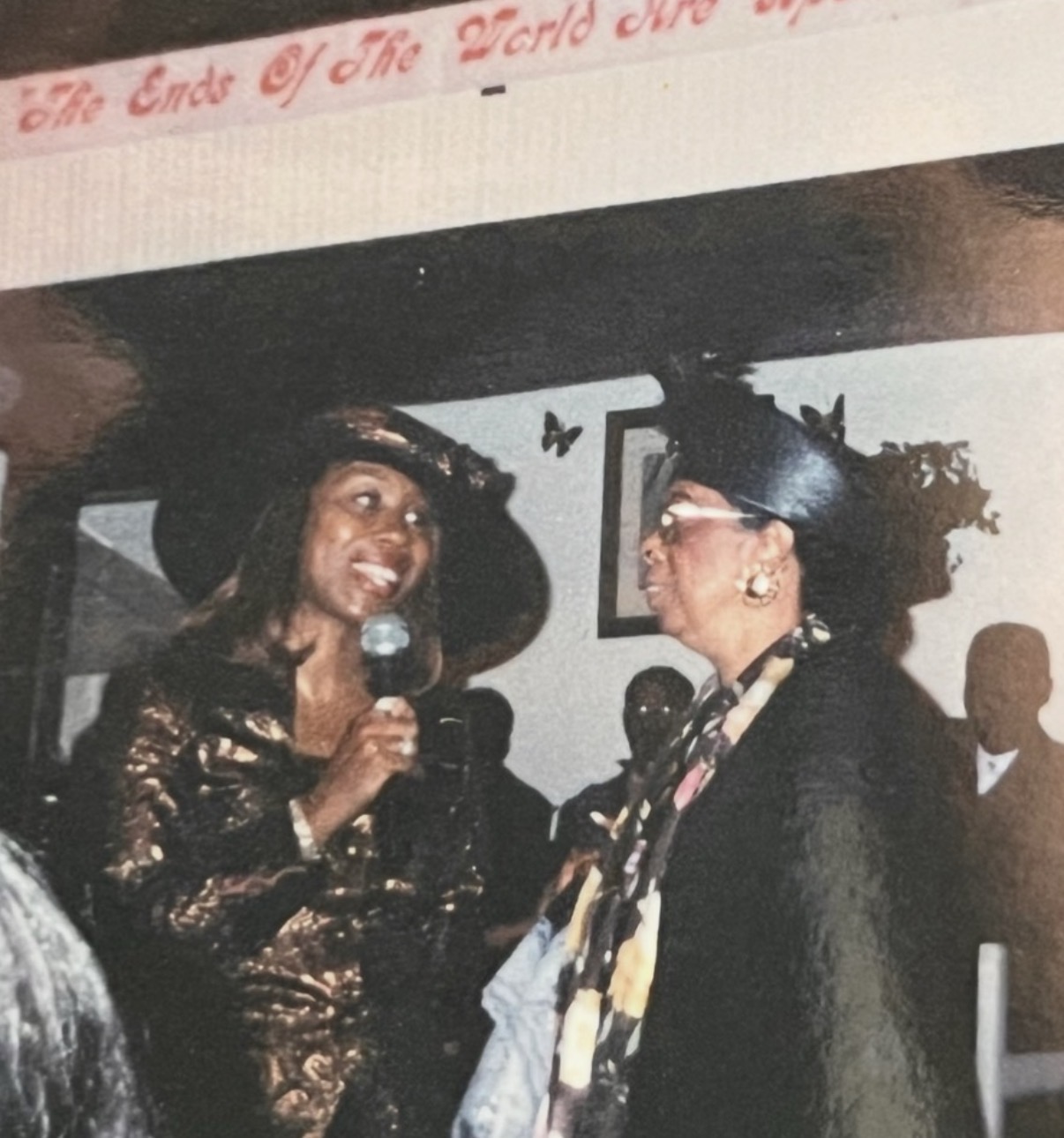 Mary on the microphone ministering alongside an elder sister in hats