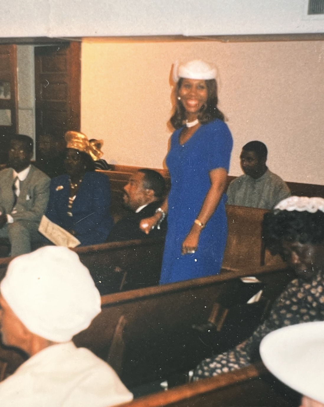 Mary in a royal blue dress and white hat addressing the congregation