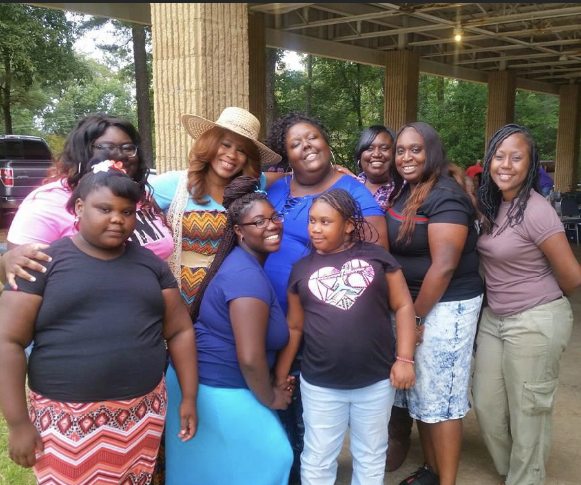 Mary in a straw hat at a family reunion surrounded by daughters, nieces, and grandchildren